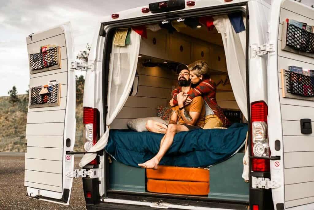 Couple On The Bed Of Campervan With Rear Doors Open