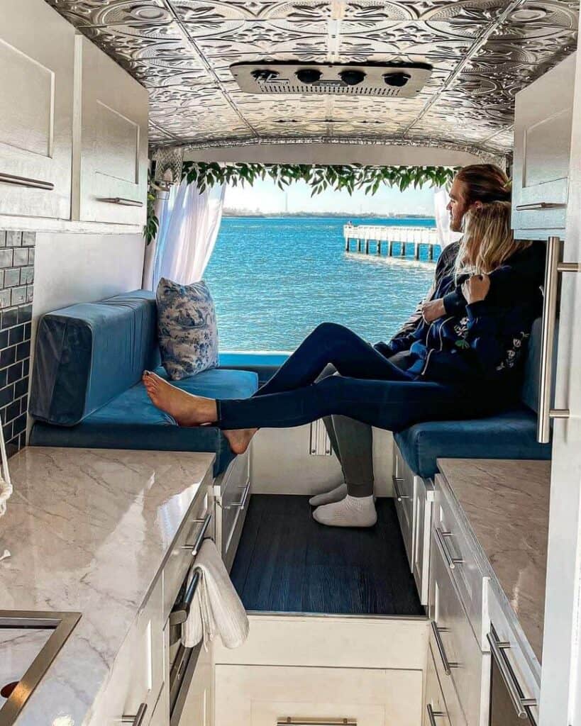 A Man And Woman Sitting On A U-Shaped Dinette That Converts To A Bed In A Campervan